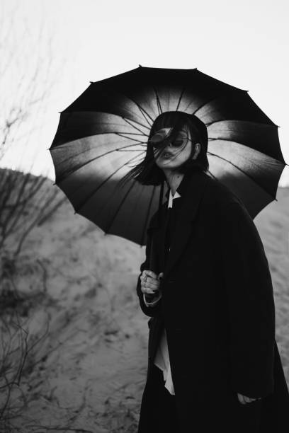 photographie en noir et blanc. fille rousse en vêtements noirs à l’extérieur. style gothique. modèle asiatique en manteau sombre avec parapluie sur la nature. bw photo. tenue élégante. sous-culture. monochrome. désaturé - gothic style photos et images de collection