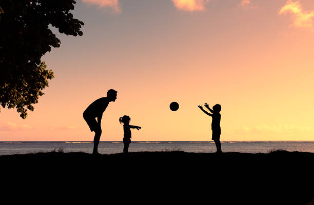 отец, сын и дочь играют с мячом в парке на закате. - men summer passing tossing стоковые фото и изображения