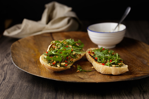 Homemade toasted ciabatta bread with vegan salsa Verde sauce, fine chopped red chilli, roasted pine nuts and rocket leaves.