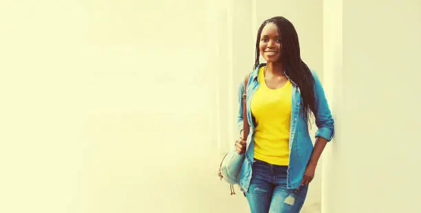 Portrait of happy smiling young african woman with backpack in casual in the city