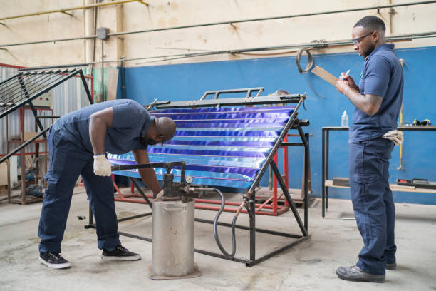 An african-american supervisor is overseeing a worker pumping water into a panel for testing at a solar panel factory