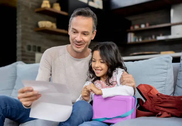 Latin American father looking very happy looking at his daughter's grades at home - lifestyle concepts