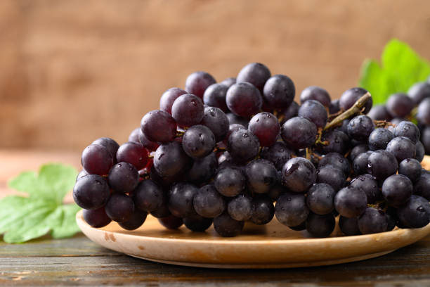 istock Red grape on wooden plate with black background 1389799668