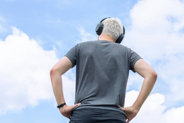 Guy with headphones standing against the sky, rear view