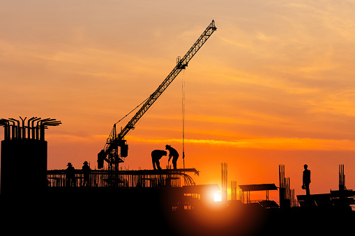 Silhouette of Foreman worker team at construction site with blurred sunset sky background