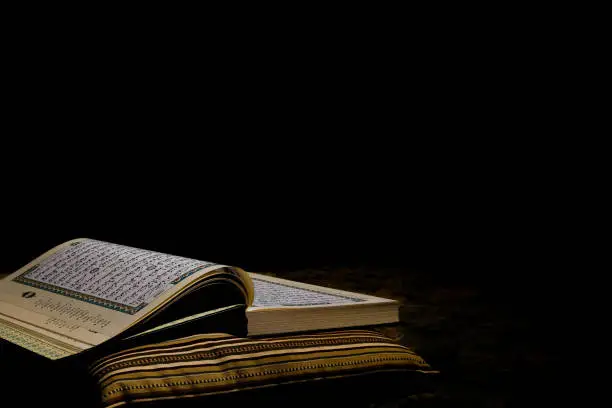 Selective focus picture of Holy Quran open on pillow at dark copyspace background