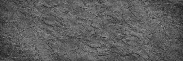 Black white rock texture. It looks like a rough concrete wall surface. Dark gray stone grunge background with space for design. Wide banner. Panoramic. Backdrop.