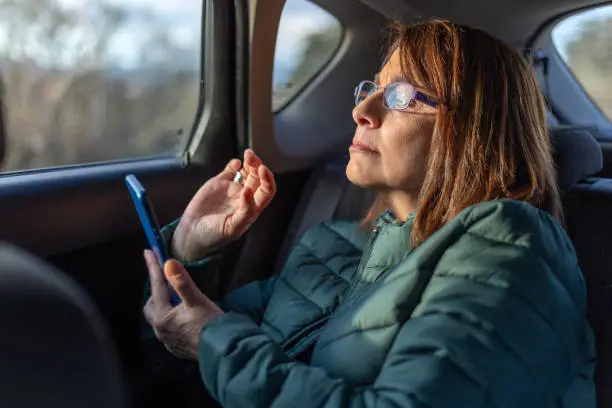 Madrid, Spain. March 5 2022. Middle-aged woman with glasses watching the screen of her mobile phone inside car with sunset light. Concept: Eye problems. Presbyopia
