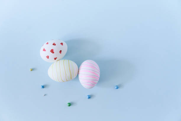 Close-up of three white Easter eggs with a pattern of hearts and waves on a blue background with decor. Orthodox Easter with a space to copy. High quality photo