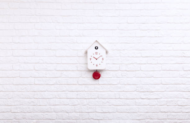 istock Cuckoo bird clock with red pendulum on a white brick wall 1389820912