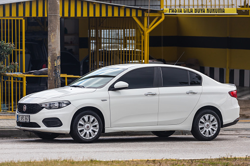 Side, Turkey – February 01 2022: white Fiat Egea is parked  on the street on a warm day against the backdrop of a fence, shop