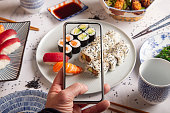 Maki rolls with smoked salmonMale hands make photography of sushi rolls with mobile phone. Top view.Young man taking a photo of a plate of sushi on a smartphone. Food photography with mobile phone.
