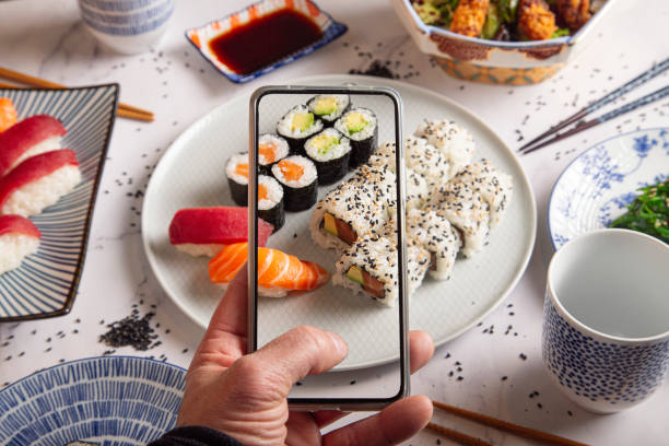 bułki maki z wędzonym łososiemmale dłonie fotografują rolki sushi telefonem komórkowym. widok z góry. młody mężczyzna robi zdjęcie talerza sushi na smartfonie. fotografia żywności z telefonem komórkowym. - foodie zdjęcia i obrazy z banku zdjęć