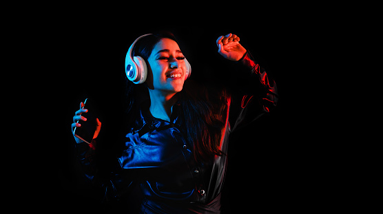 latin young woman with headphones listening to music over color neon and black background in Mexico Latin America