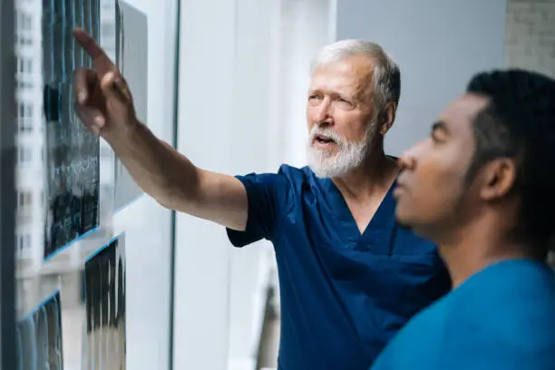 Photo of Close-up of team multi-ethnic doctors talking together history disease using MRI scan of patient during medical meeting standing near window.