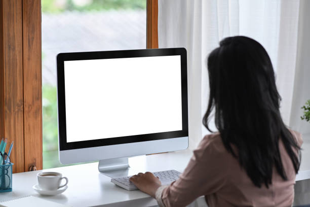 istock Rear view of businesswoman using computer at bright modern workplace. 1389833304