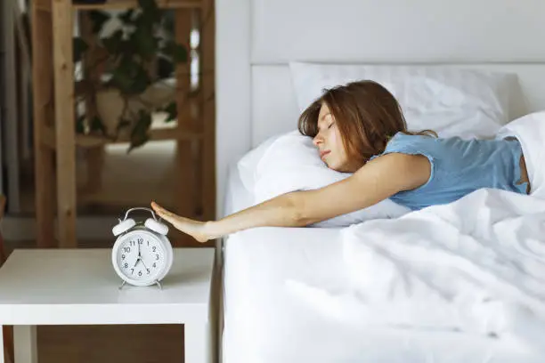 Photo of Woman sleep on the bed turns off the alarm clock wake up at the morning, Selective focus.Side view