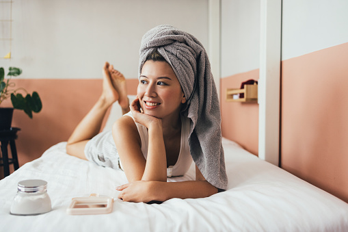 A happy Thai woman resting on her bed after having a shower in the morning.
