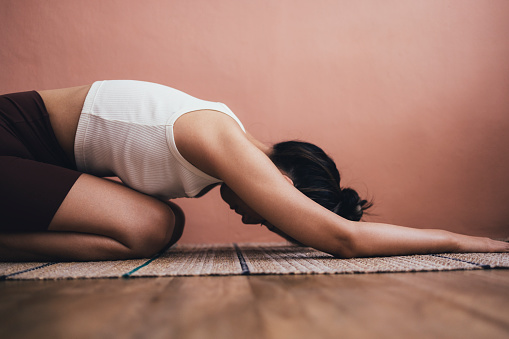 An anonymous Asian woman holding the child's pose while doing yoga on a mat.