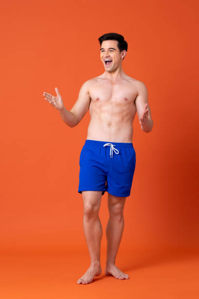 고립 된 스튜디오 색상 배경에 여름 짧은 바지를 입은 놀란 젊은 셔츠가없는 백인 남자 - men swimwear full length fashion model 뉴스 사진 이미지