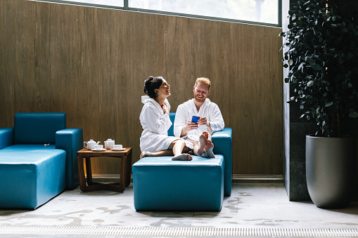Young couple relaxing in the spa centre, the are laughing at something on the smartphone.