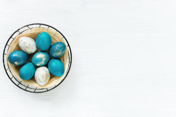 istock Easter basket with colored blue and gold eggs on a white wooden background with copy space. Horizontal easter banner with nest with eggs in minimal loft style. Modern ideas for Easter design. 1389839332