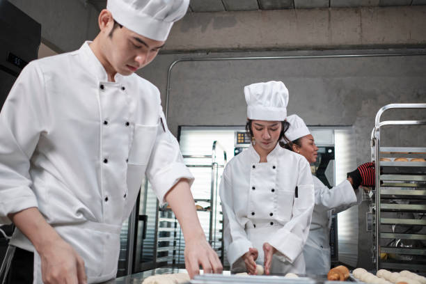 istock Chefs team in uniforms prepare to bake bread and pastry in stainless kitchen. 1389839576