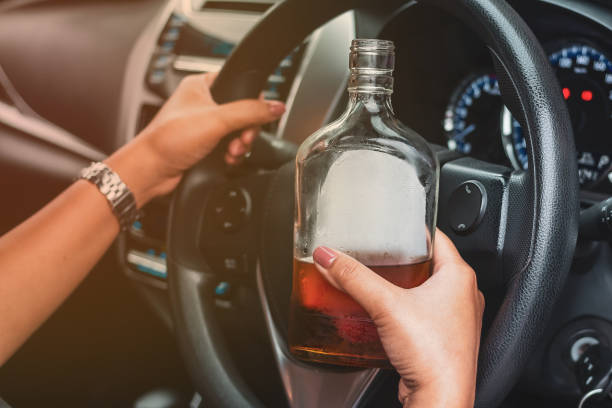 Drunk female driver with alcohol bottles sitting behind the wheel, not drinking and driving. stock photo
