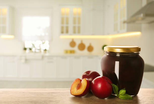 Jar with pickled plums on wooden table in kitchen. Space for text
