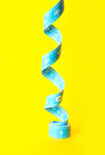 istock Light blue measuring tape on yellow background, closeup 1389843925