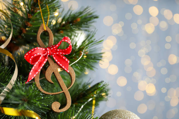 istock Wooden music note with red bow hanging on Christmas tree against blurred lights. Space for text 1389844279