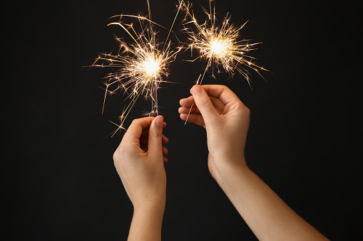 Woman holding bright burning sparklers on black background, closeup