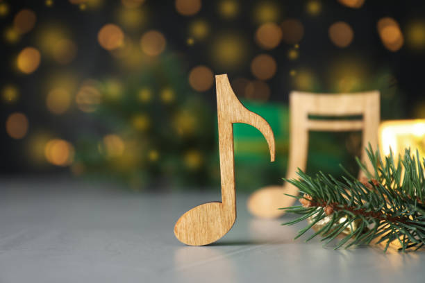 istock Wooden music note and fir branches on light grey table against blurred Christmas lights 1389845780