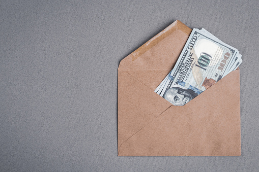 Dollar bills in a paper envelope on a gray background. Bonus, reward, benefits concept