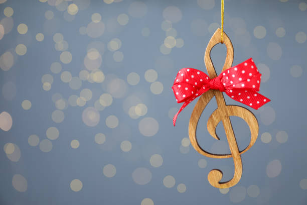 istock Wooden music note with red bow hanging on light blue background with Christmas lights. Space for text 1389846692