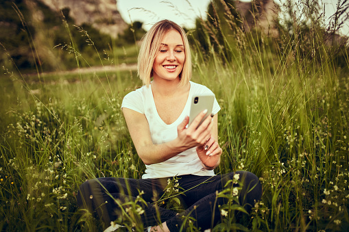 Happy woman sitting on the grass meadow using smartphone