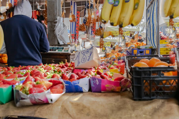 Strawberries for sale in Birkhadem's covered market of fruits and vegetables. Algiers, Algeria- Mars 14, 2022: close-up strawberry boxes with the price in arabic. Oranges, bananas, dates and an old balance. algiers stock pictures, royalty-free photos & images