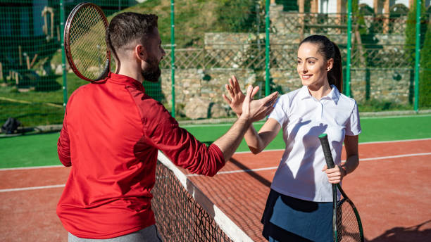 hombre y mujer jóvenes se dan la mano antes de jugar al tenis. retrato de jóvenes y hermosas jugadoras con ropa deportiva elegante dándose la mano después de un partido deportivo al aire libre. estilo de vida activo. - tennis couple women men fotografías e imágenes de stock