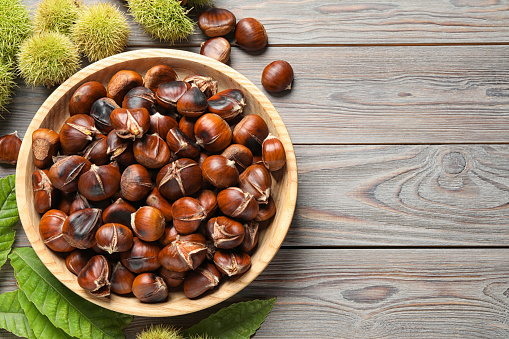 Delicious roasted edible chestnuts on brown wooden table, flat lay. Space for text