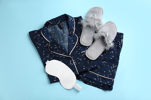 House slippers, sleeping mask and pajamas on light blue background, flat lay