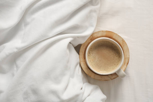 istock Cup of aromatic coffee on bed with soft blanket, top view. Space for text 1389851814