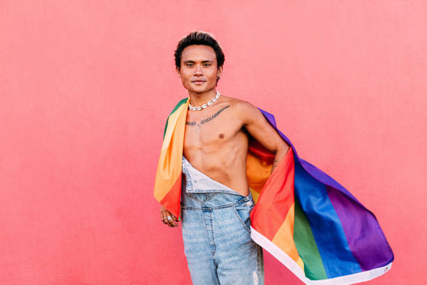 istock Young man wrapped in rainbow LGBT flag standing outdoors and looking at camera 1389853951