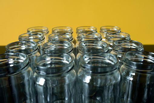 Frontal shot of empty glass jars lined up in a row on a yellow background. Selected focus top of jar in front.