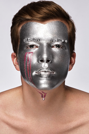 Young man with art creative art make-up with silver paint on his face. Beauty face. Picture taken in the studio on a white background.