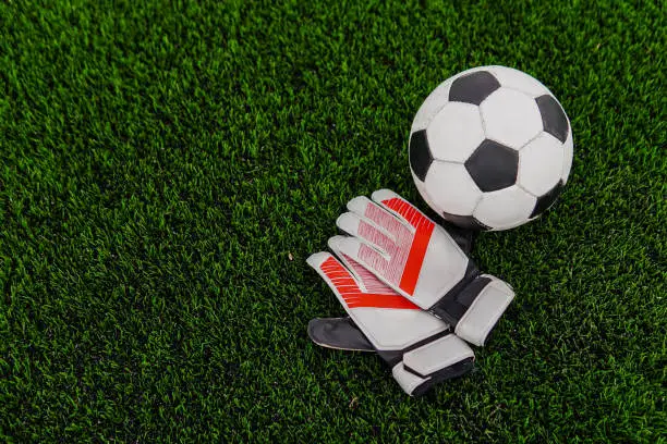Soccer ball and goalkeeper gloves on football field. Copy space.