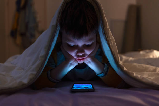 istock Little boy on cell phone under duvet. 1389857163