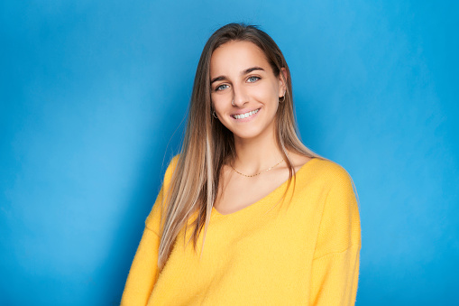 Portrait of young girl looking at camera smiling with yellow sweater and blue background