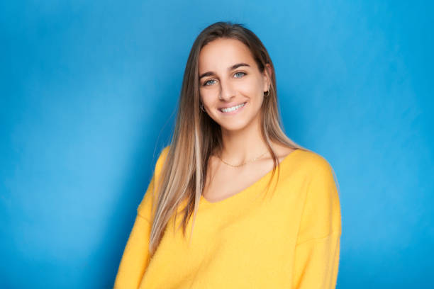 Portrait of young girl looking at camera smiling with yellow sweater and blue background stock photo