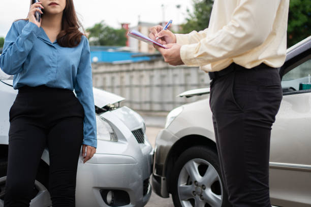 아시아 여성 운전자는 사고 후 보고 청구 양식에 손상된 자동차와 고객 확인을 조사하기 위한 보험 대리점에 이야기합니다. 보험 및 자동차 교통 사고의 개념. - 교통사고 뉴스 사진 이미지