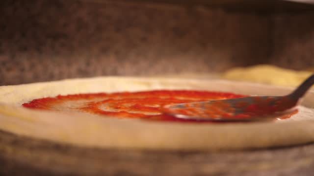 Chef spreads red the tomato sauce over the pizza blank dough cooking in italian pizzeria